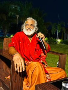 The master joyfully shares profound wisdom holding a microphone during a serene evening AtmaNambi spiritual service gathering.